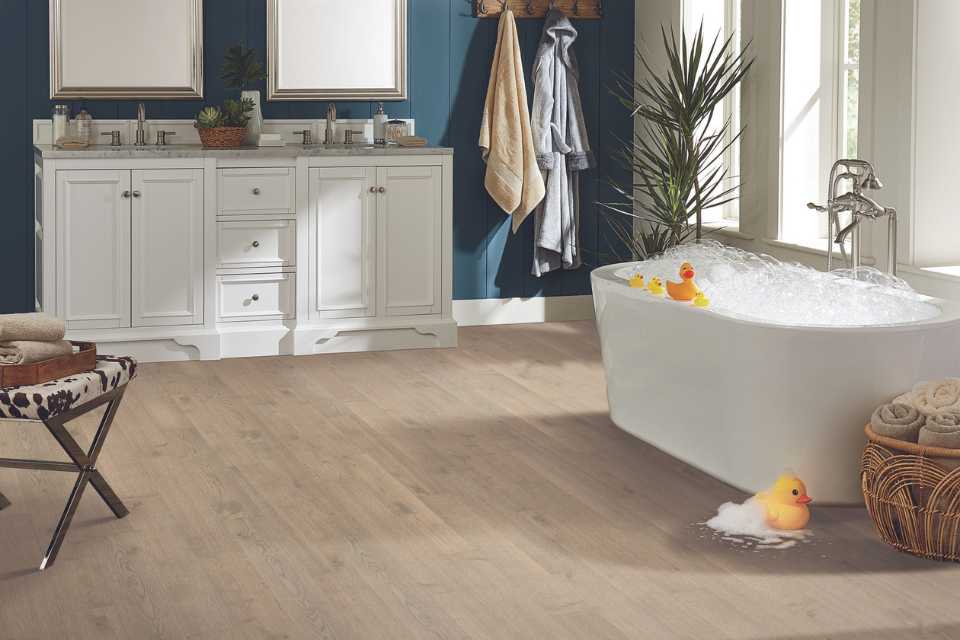 light colored engineered hardwood in bathroom with deep soak tub overflowing with bubbles on floor